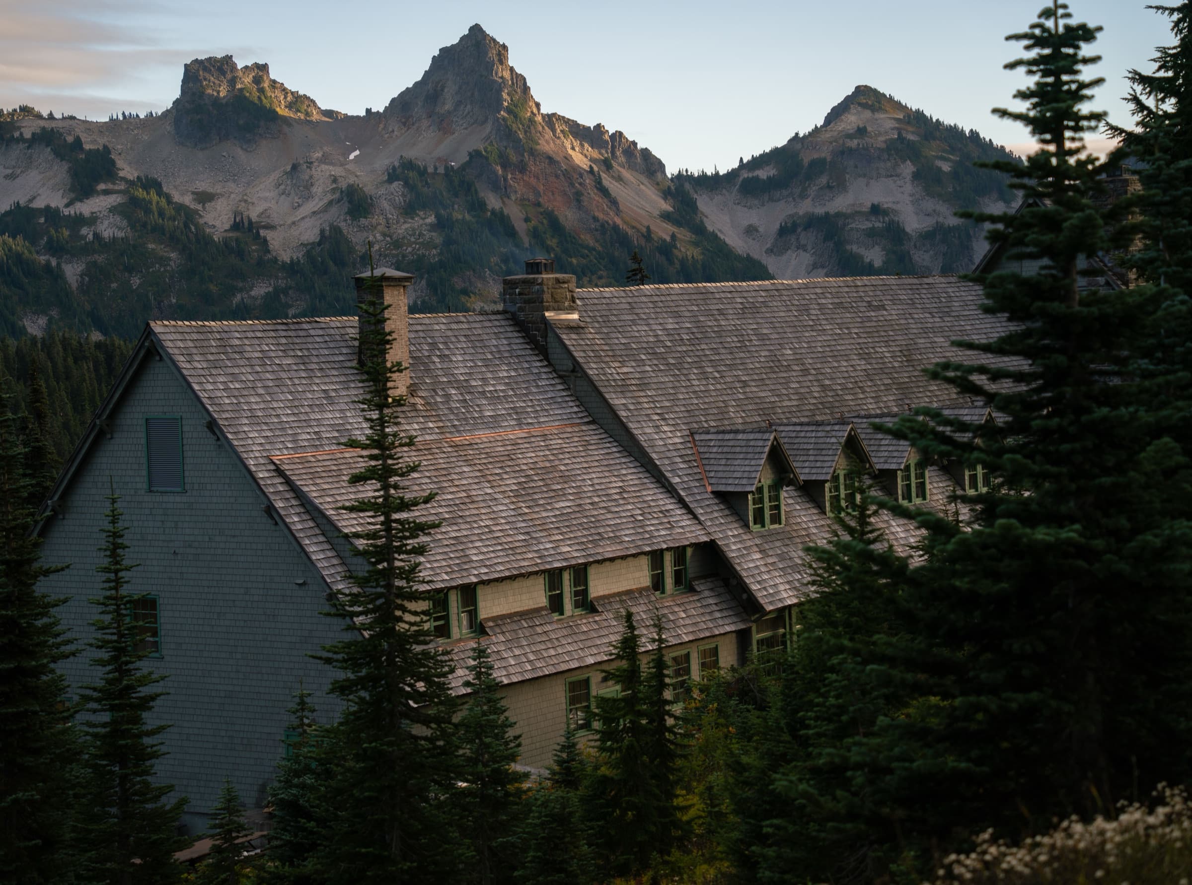 A backcountry lodge at dusk, set below a jagged mountain ridge.