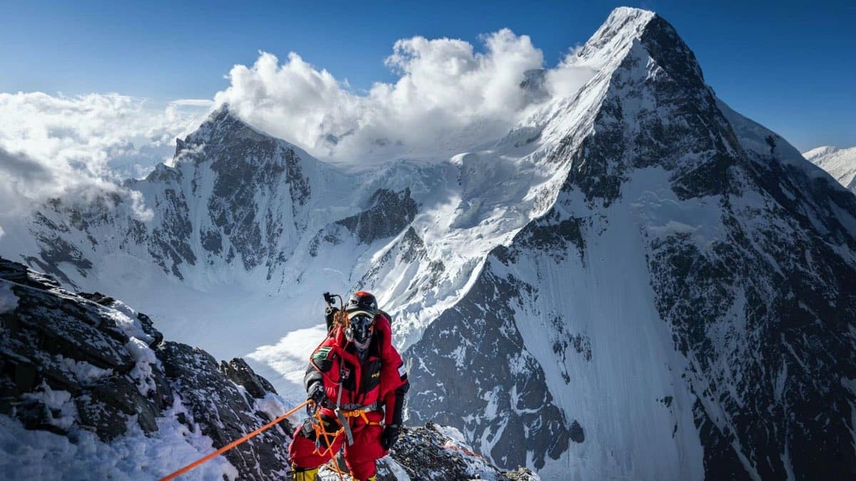 A climber on a snow ridge below a high granite face