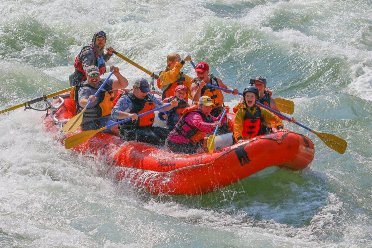 A full raft of paddlers punching through a whitewater wave